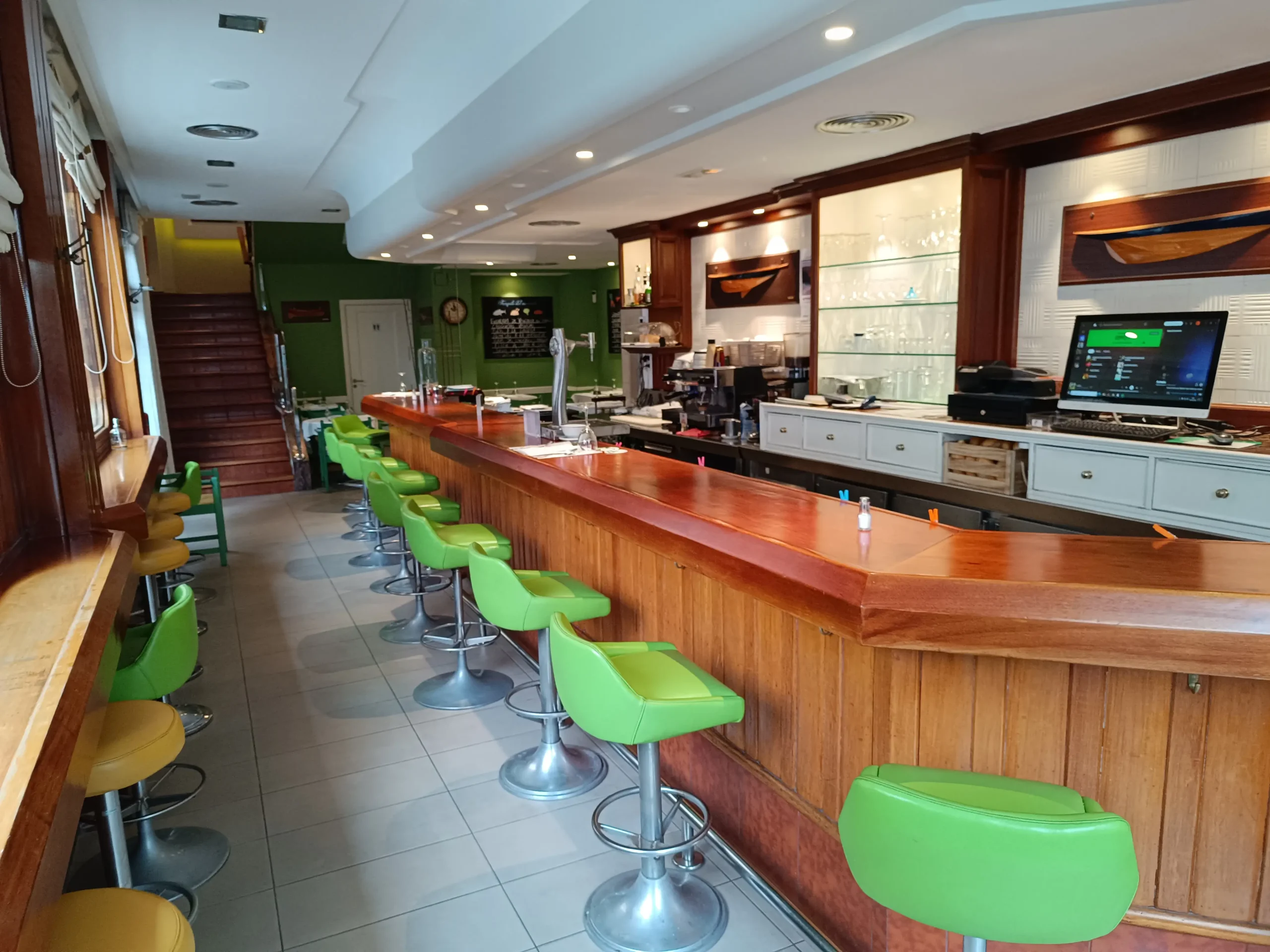 Vista del interior del bar del Restaurante Samoa, con la barra de madera y sillas verdes.